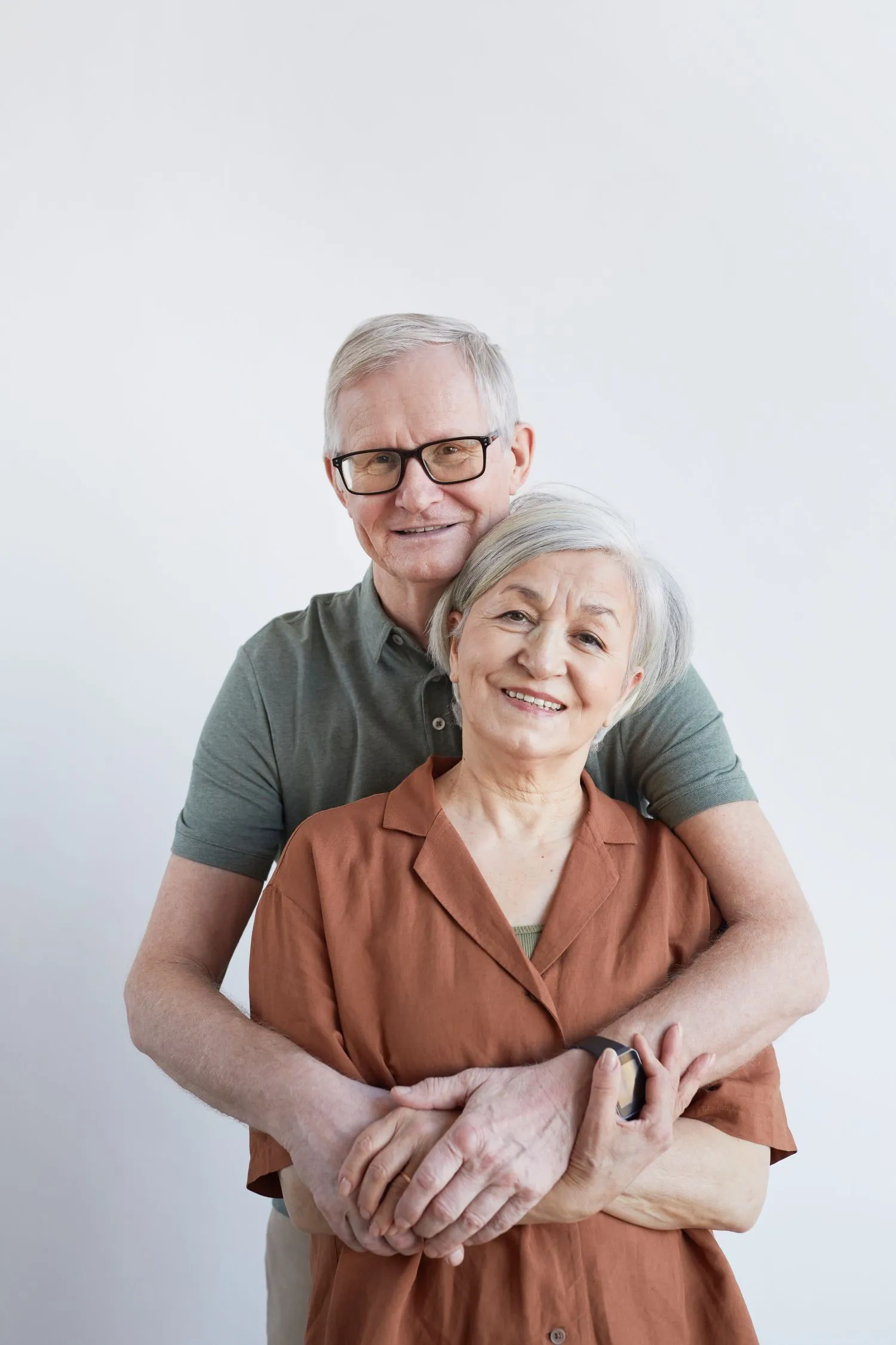 vertical-portrait-loving-senior-couple-embracing-looking-camera-while-standing-against-white-background